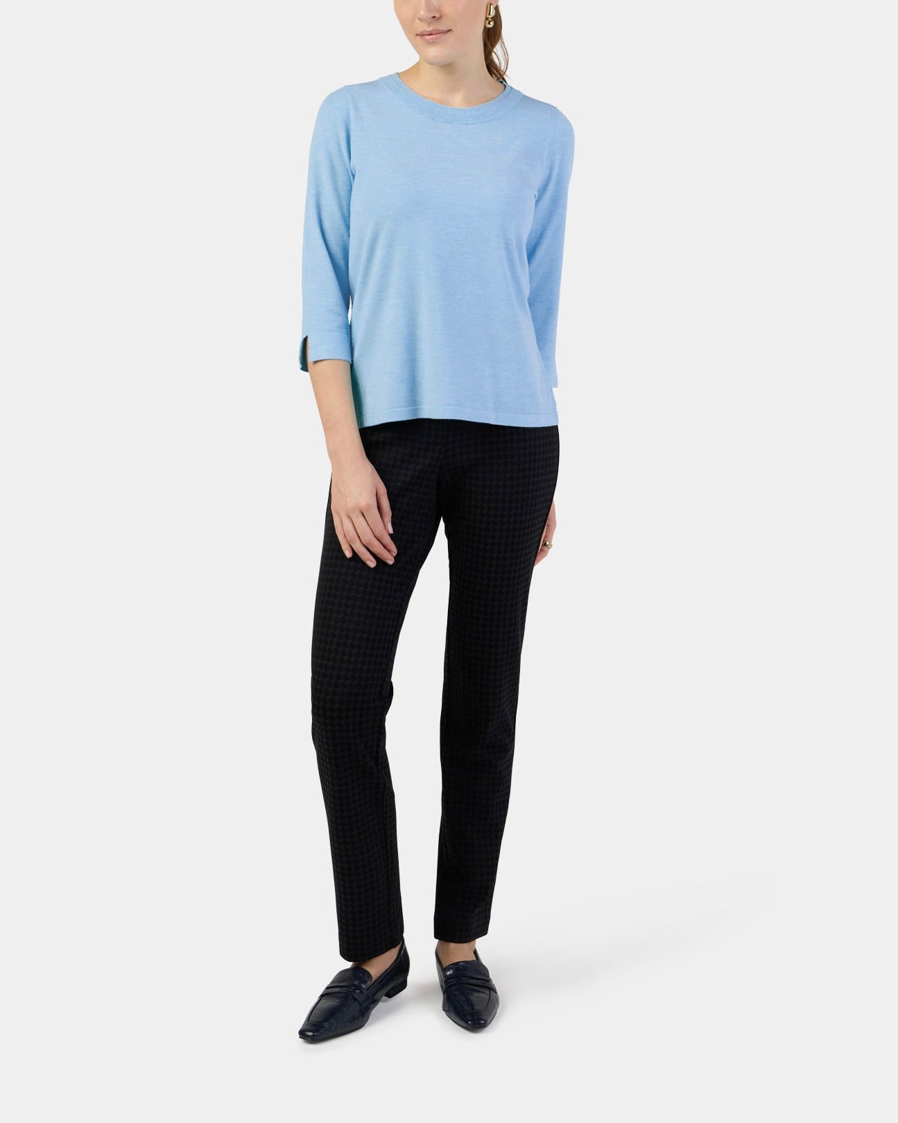Woman wearing a light blue sweater and black pants on a white background