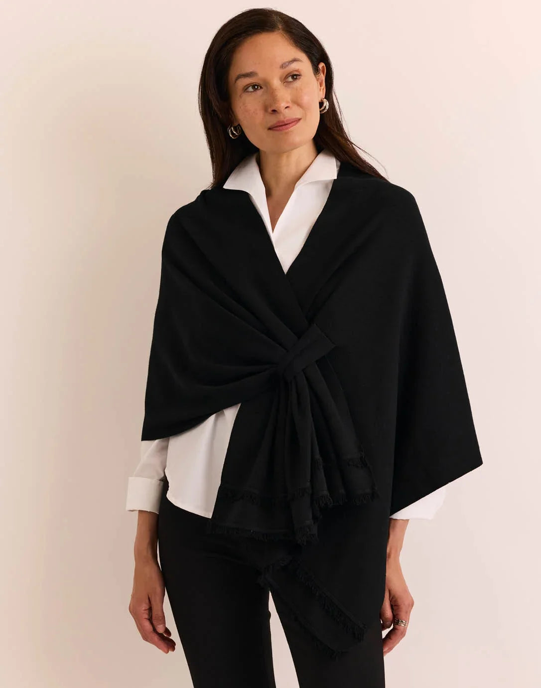 A woman modeling a black wrap shawl by The H Edition Mabel Tab Fringe Wrap