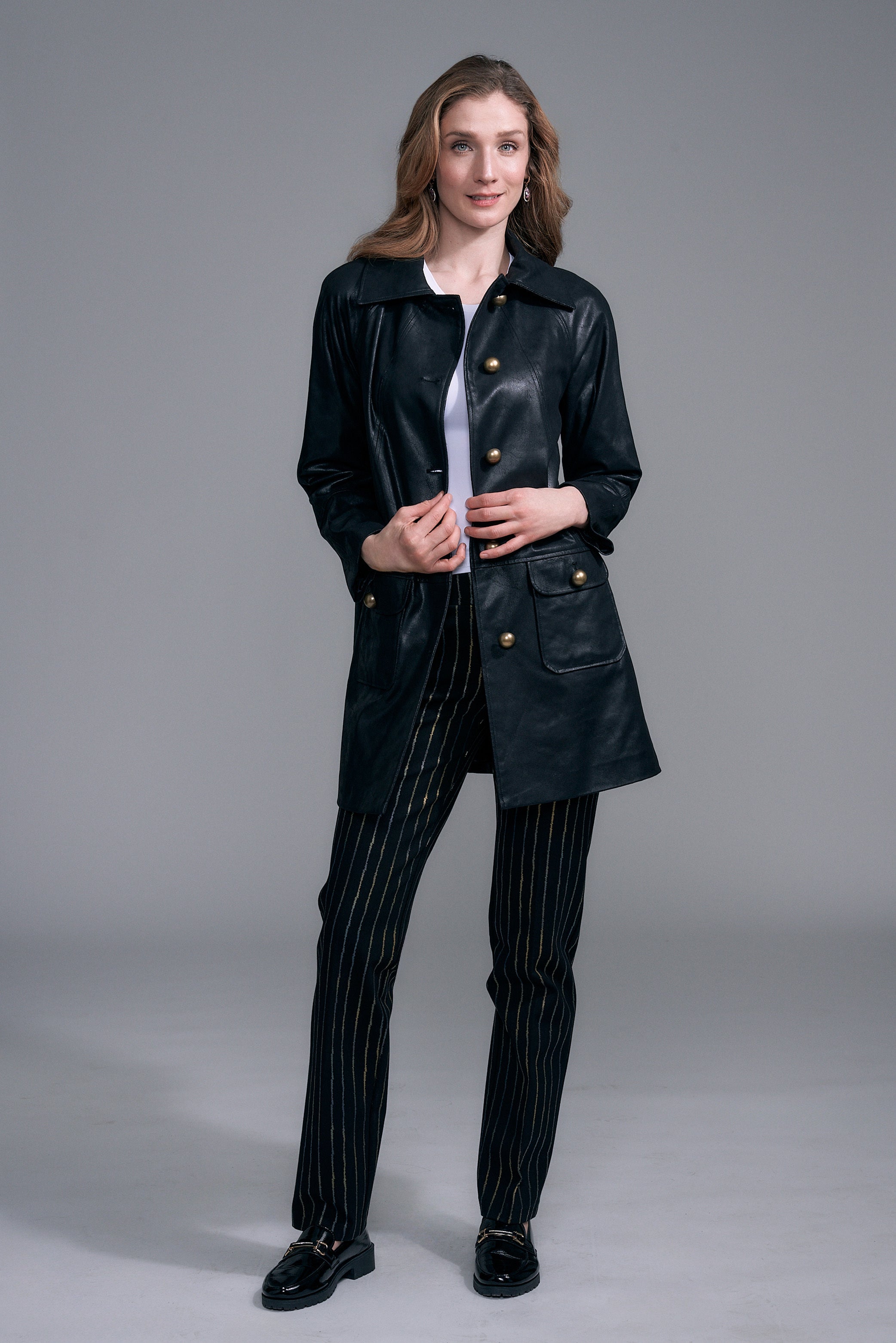 A woman modeling a black leather coat with gold-tone buttons by insight Vegan Leather Car Coat