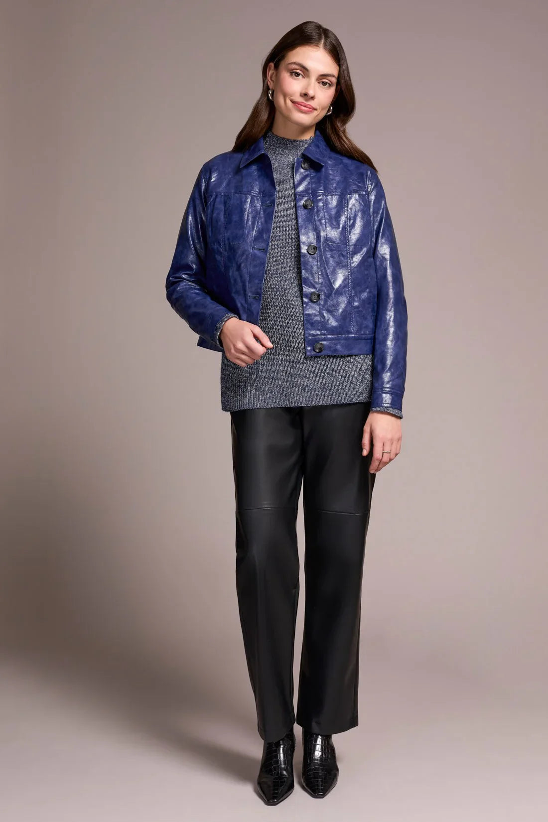 Woman wearing a blue jacket, gray sweater, and black pants on a beige background