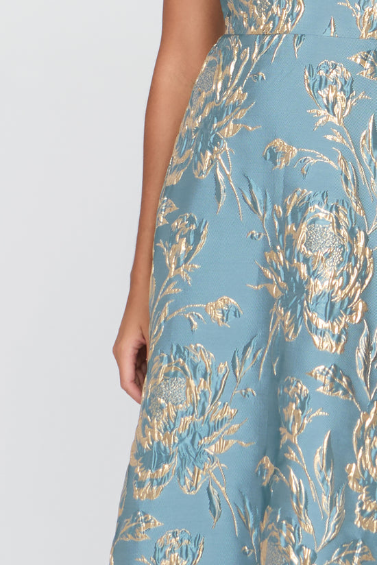 Close-up of a blue dress with gold floral pattern on a white background