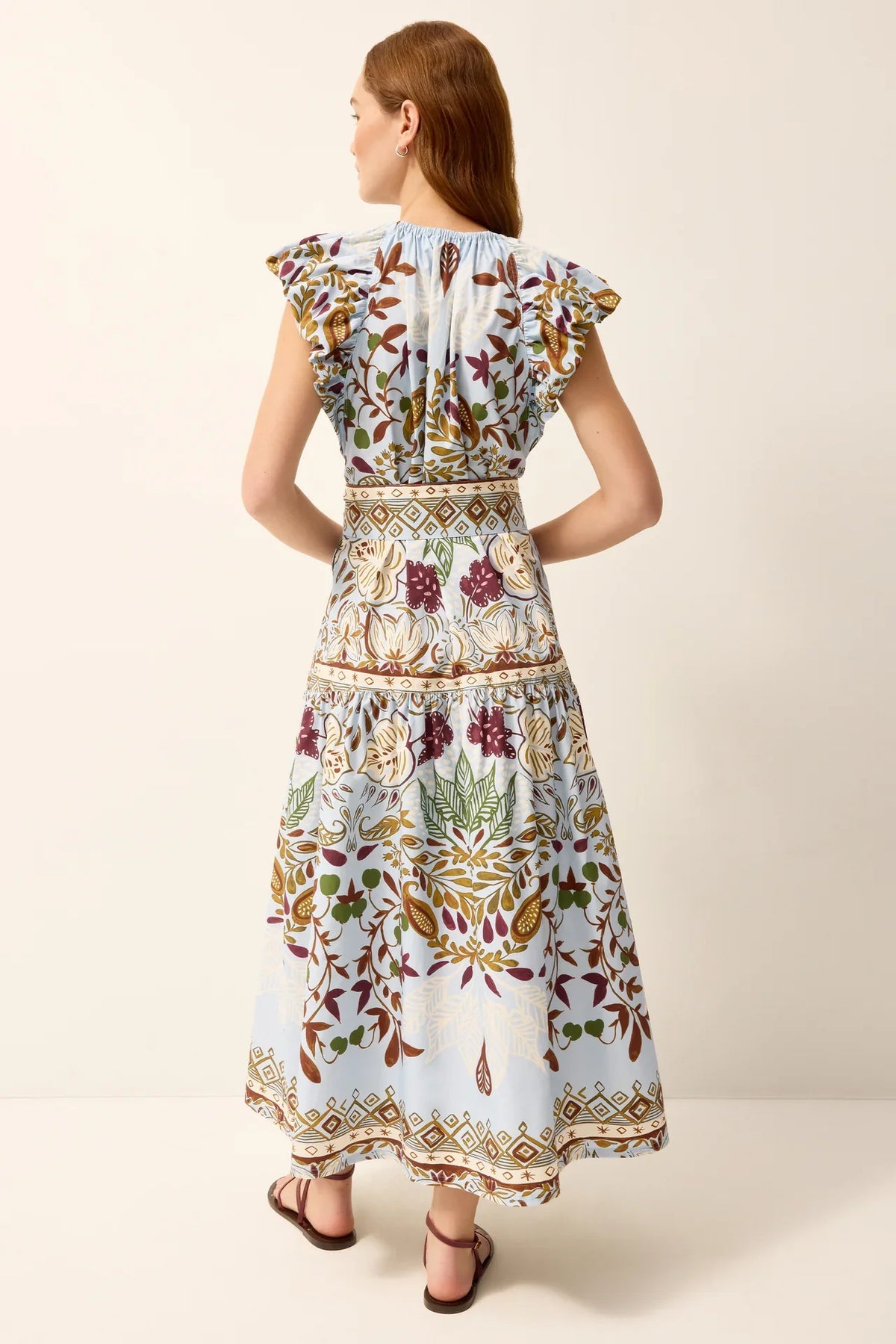 Marie Oliver Leena Dress in natural fabric with a flowy silhouette, shown on a mannequin with a leafy branch background.