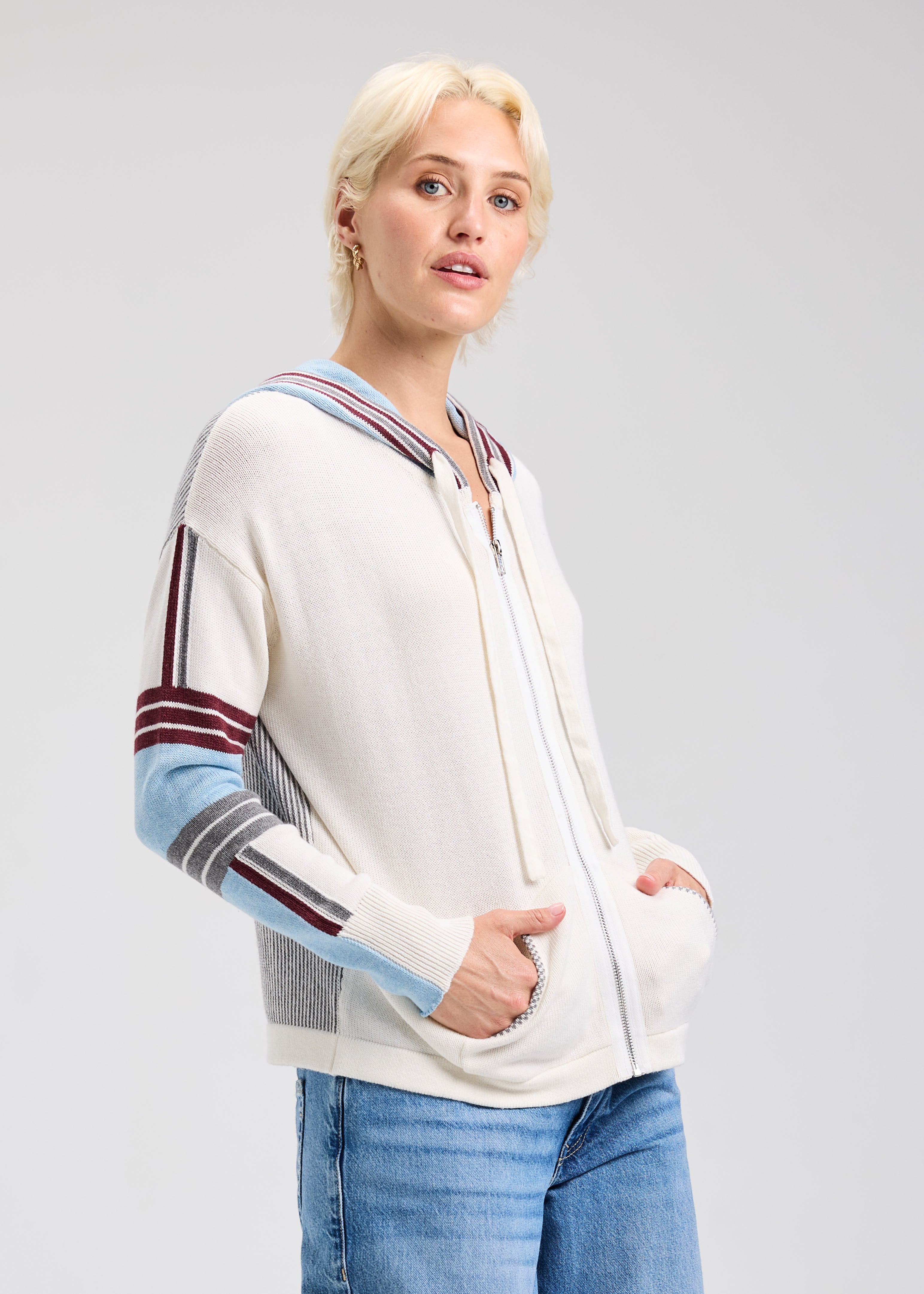 Woman wearing a white cardigan with colorful stripes on a light gray background