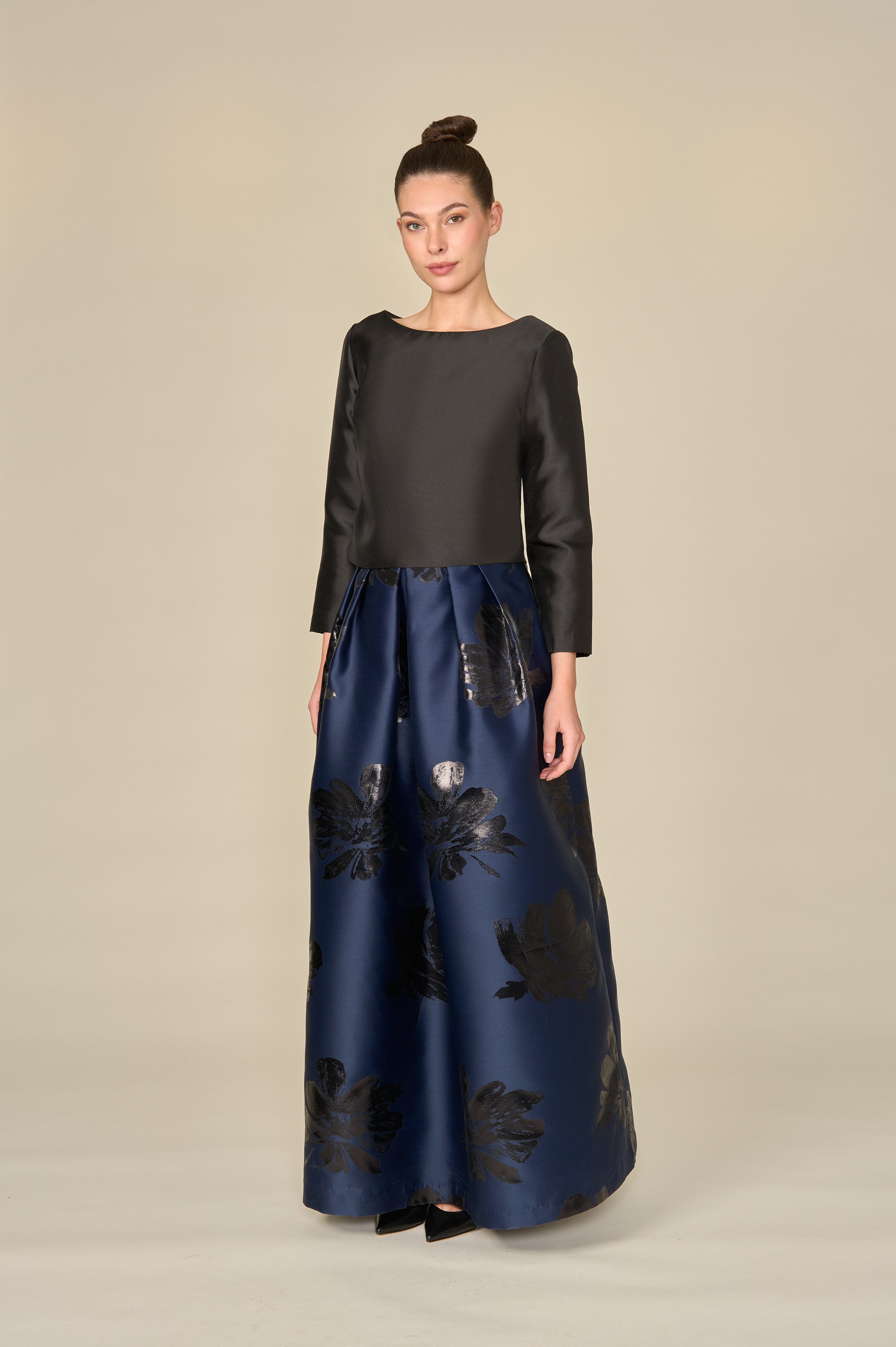 Woman wearing a black top and navy blue pants with floral patterns on a beige background