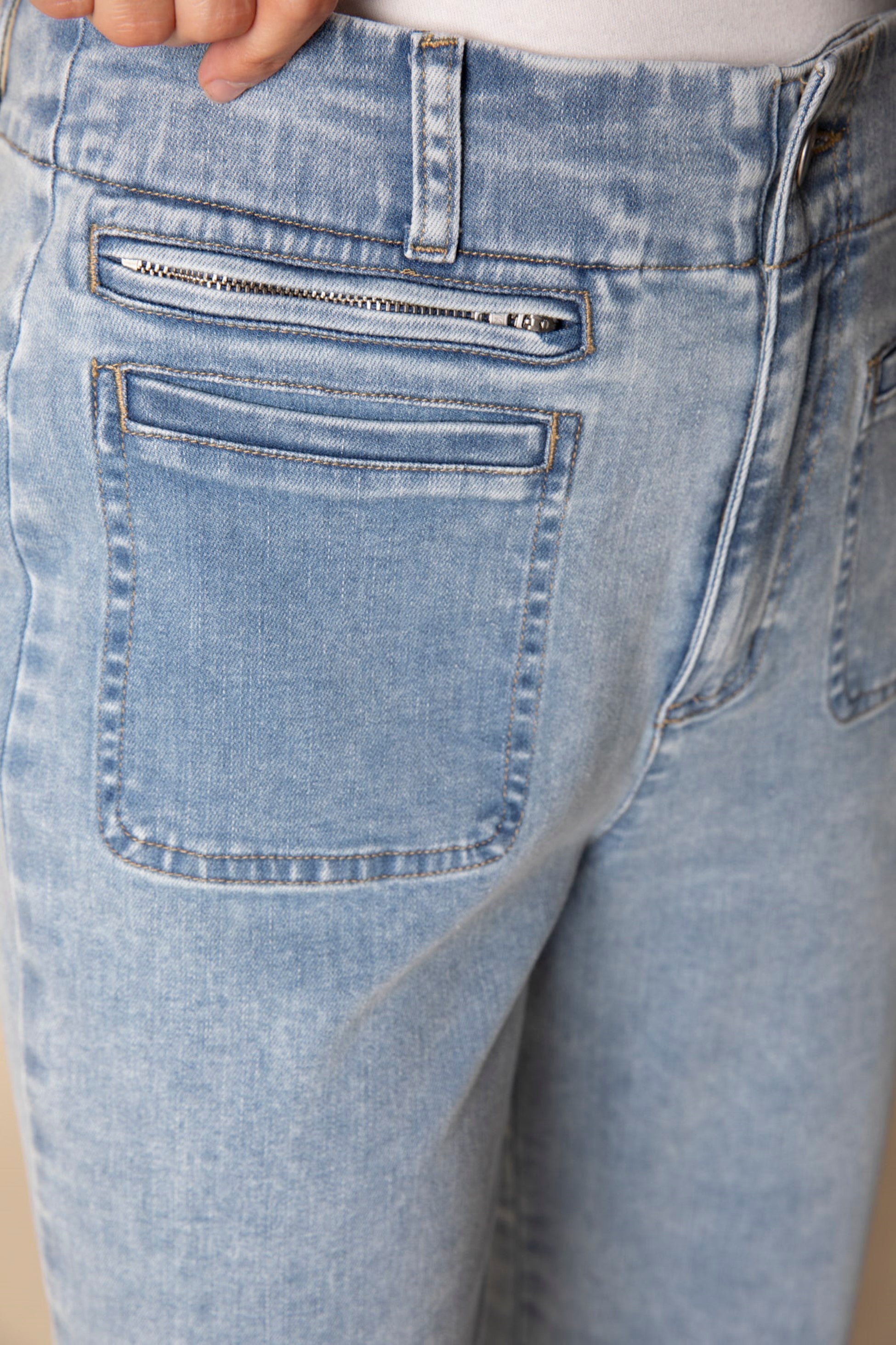 Close-up of light blue jeans with a focus on the back pocket and zipper area.