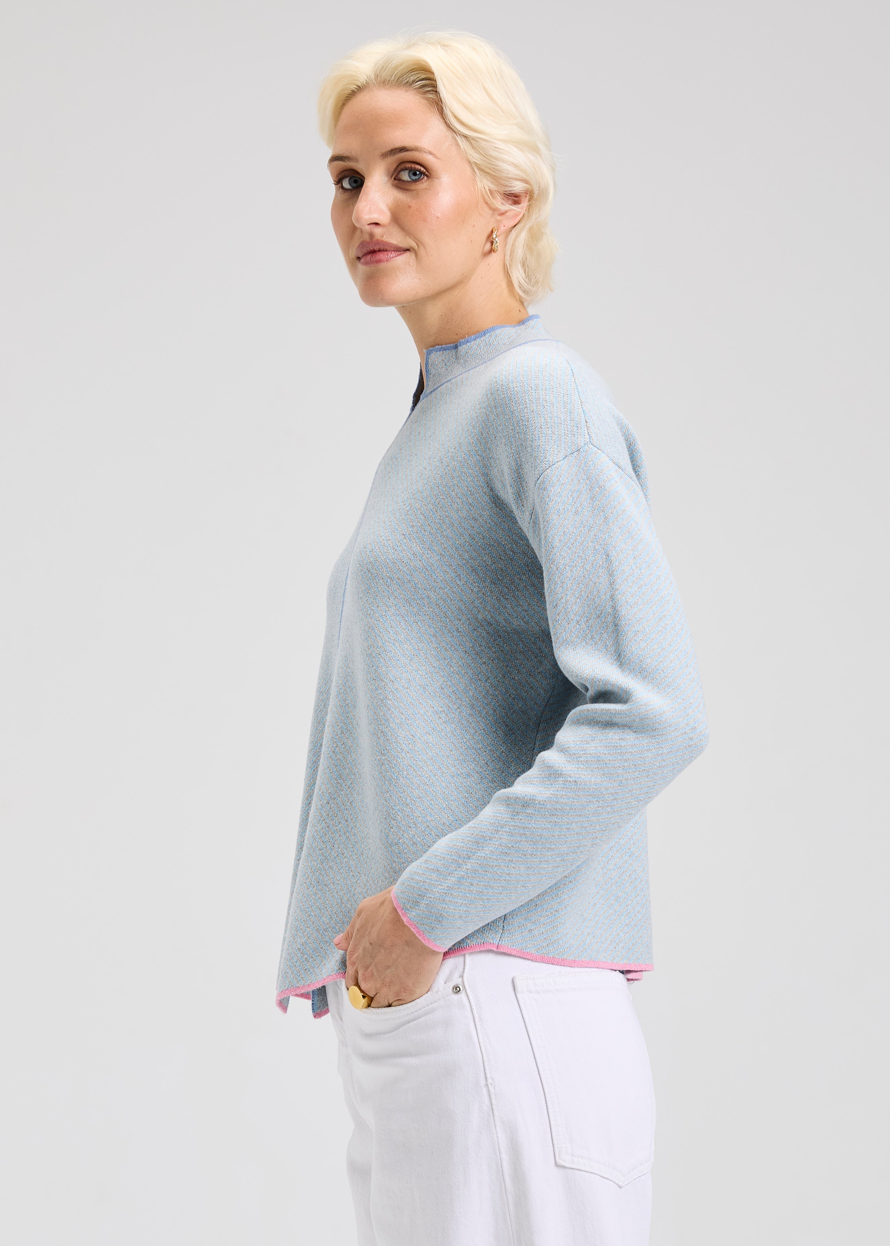 Woman wearing a light blue sweater with dark blue and pink details with a plain background