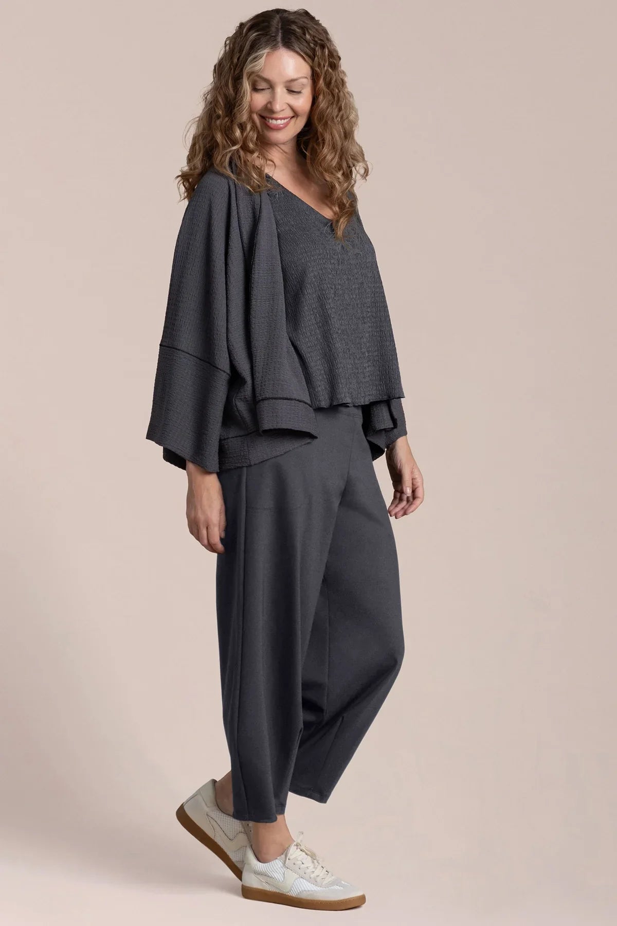 Woman wearing a gray outfit with a draped top and wide-leg pants on a beige background