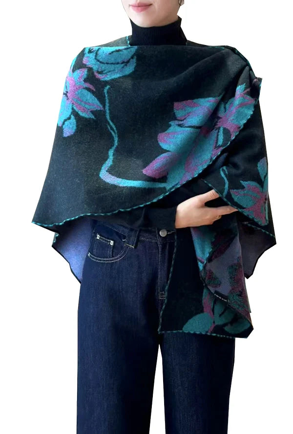 Person wearing a dark purple and green poncho with floral patterns over a black turtleneck and blue jeans on a white background.