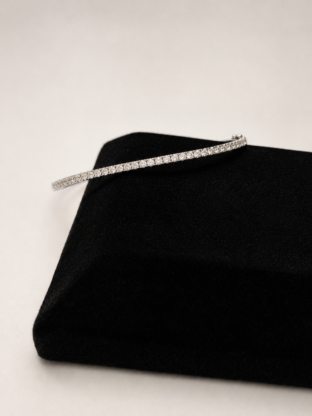 A slim silver tennis bracelet paved with small clear stones, displayed on a black velvet jewelry box against a light gray background.