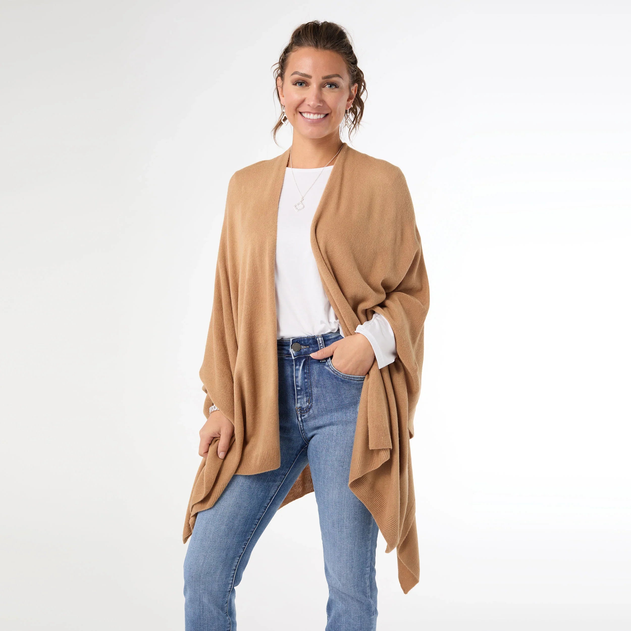 Woman wearing a beige cardigan, white shirt, and blue jeans on a white background