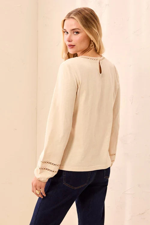 A woman wearing a light cream long-sleeve top with decorative eyelet lace detailing at the neckline and cuffs by tribal Cotton Slub Eyelet Trim Long Sleeve Knit Top