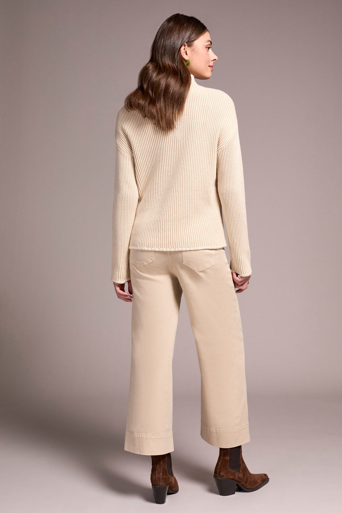 Woman wearing a beige sweater and pants against a plain background