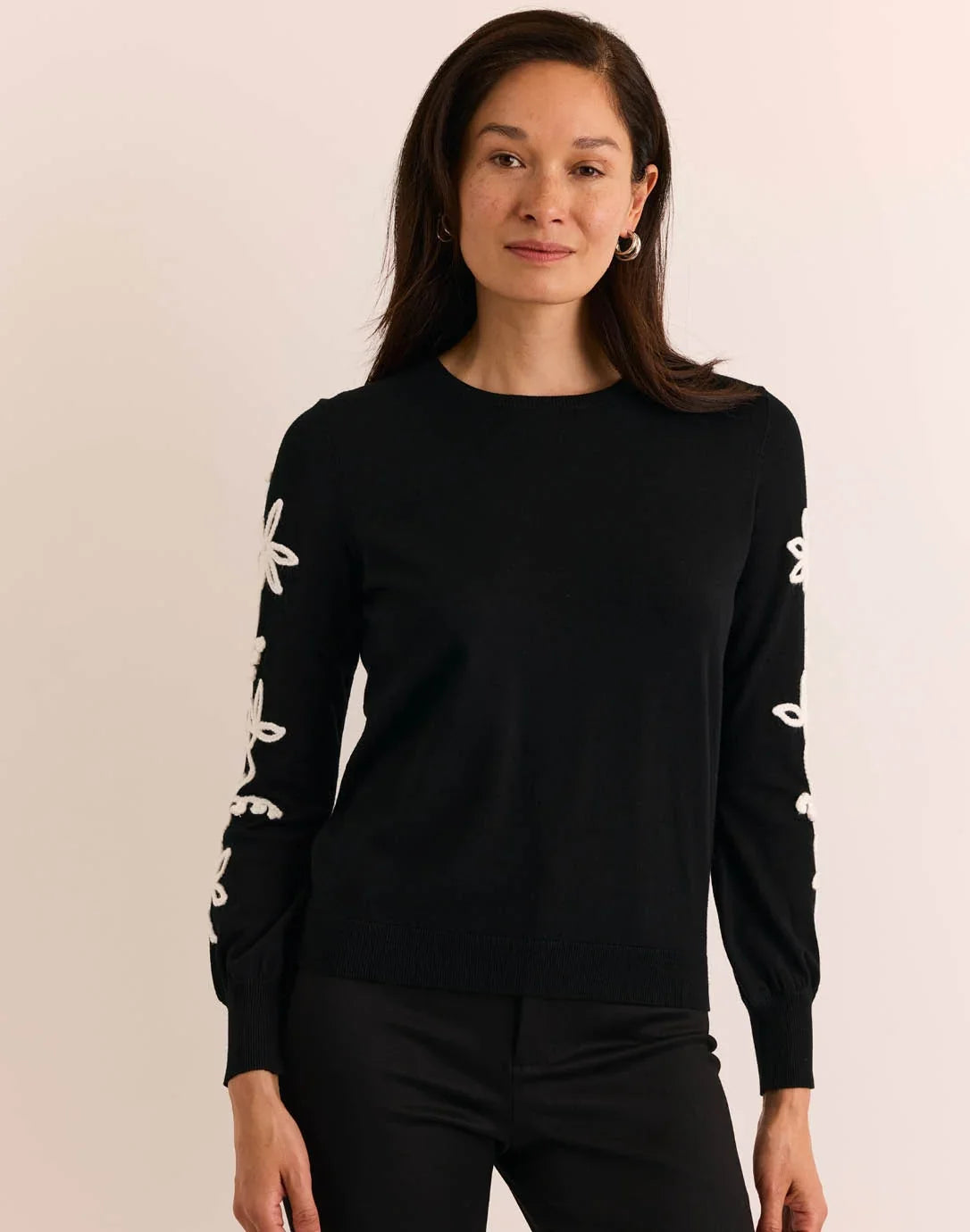Woman wearing a black sweater with white floral patterns, The H Edition  Kannon Long Sleeve Embroidered Sweater
