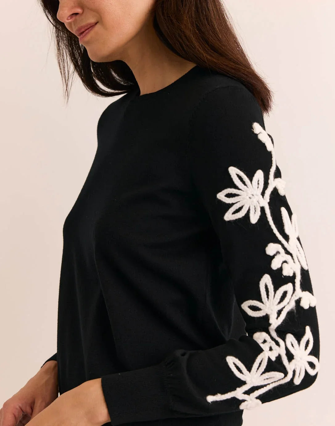Woman wearing a black sweater with white floral patterns, The H Edition  Kannon Long Sleeve Embroidered Sweater