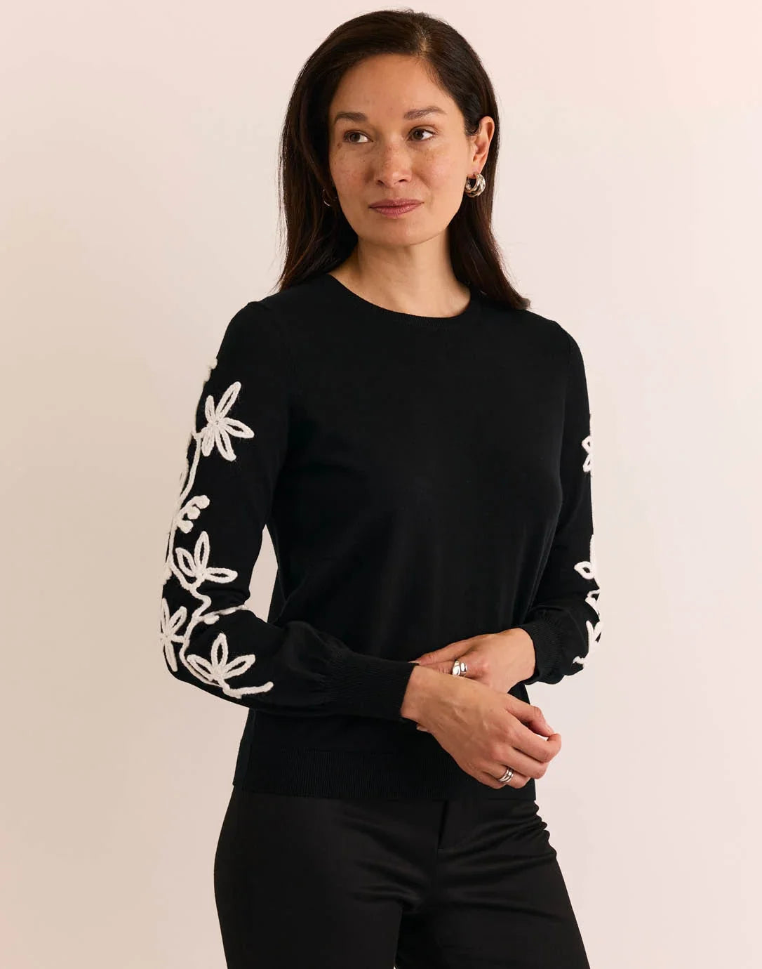 Woman wearing a black sweater with white floral patterns, The H Edition  Kannon Long Sleeve Embroidered Sweater