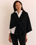 A woman modeling a black wrap shawl by  The H Edition Mabel Tab Fringe Wrap