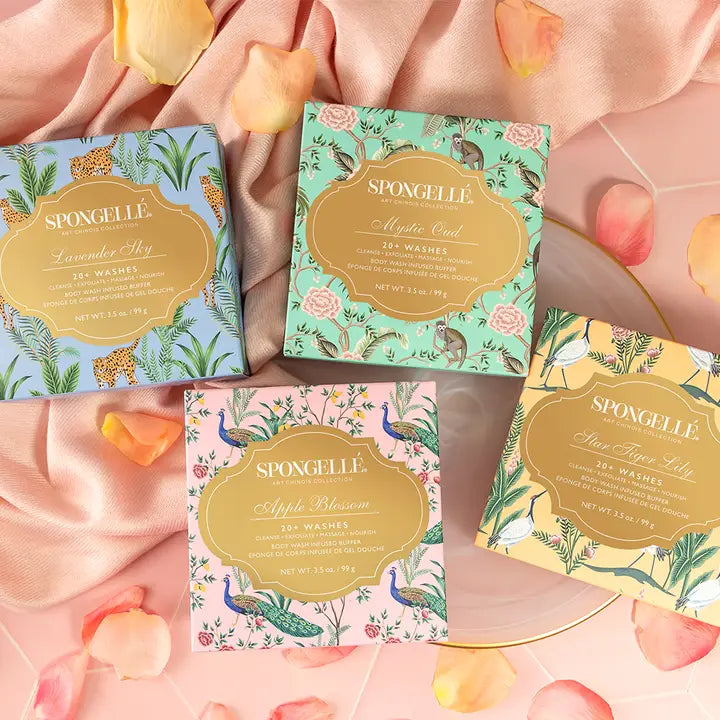 Four boxes of Spongelle body buffer soap with floral designs on a pink fabric background.