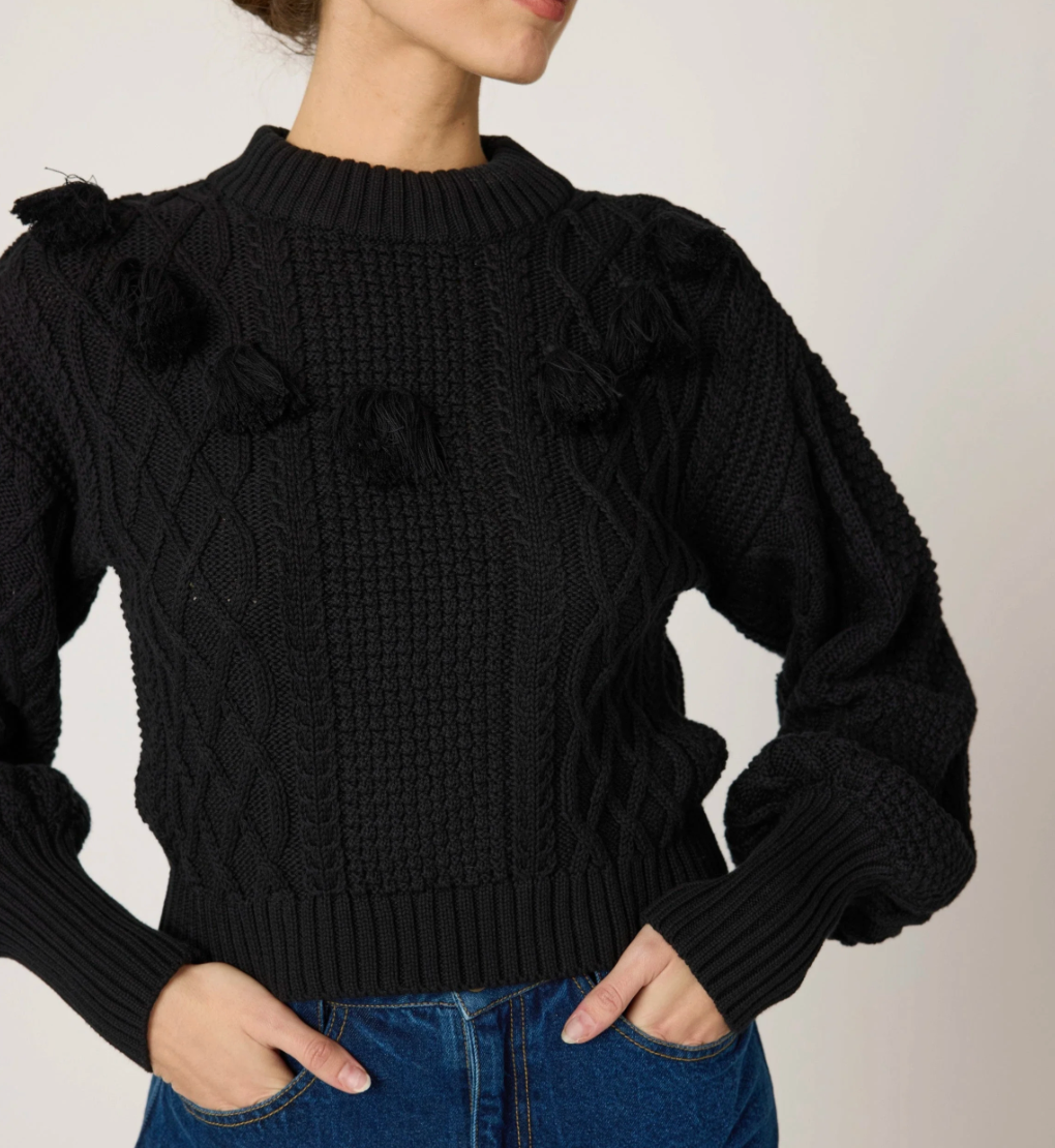 detail shot woman wearing a black knit sweater, textured with tassel details around the top