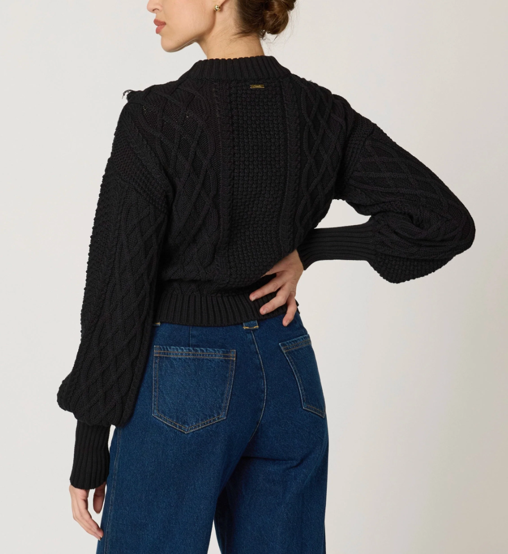 back view of woman wearing a black knit sweater, textured with tassel details around the top