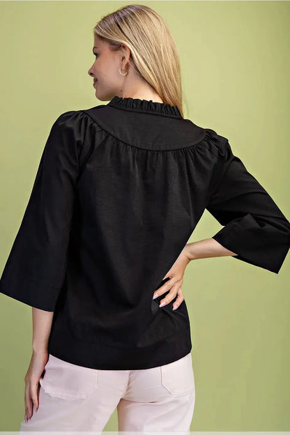 A woman modeling a black three-quarter sleeve top with a V-neckline Black Ruffled Neck Blouse