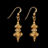 A pair of gold dangle earrings with textured, leaf-like beaded drops and a small clear stone accent, shown against a solid black background.