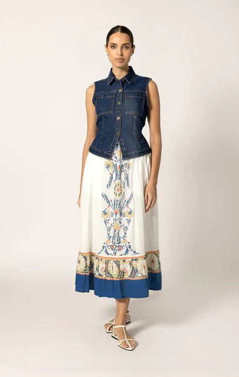 Woman wearing a denim vest over a patterned dress on a plain background