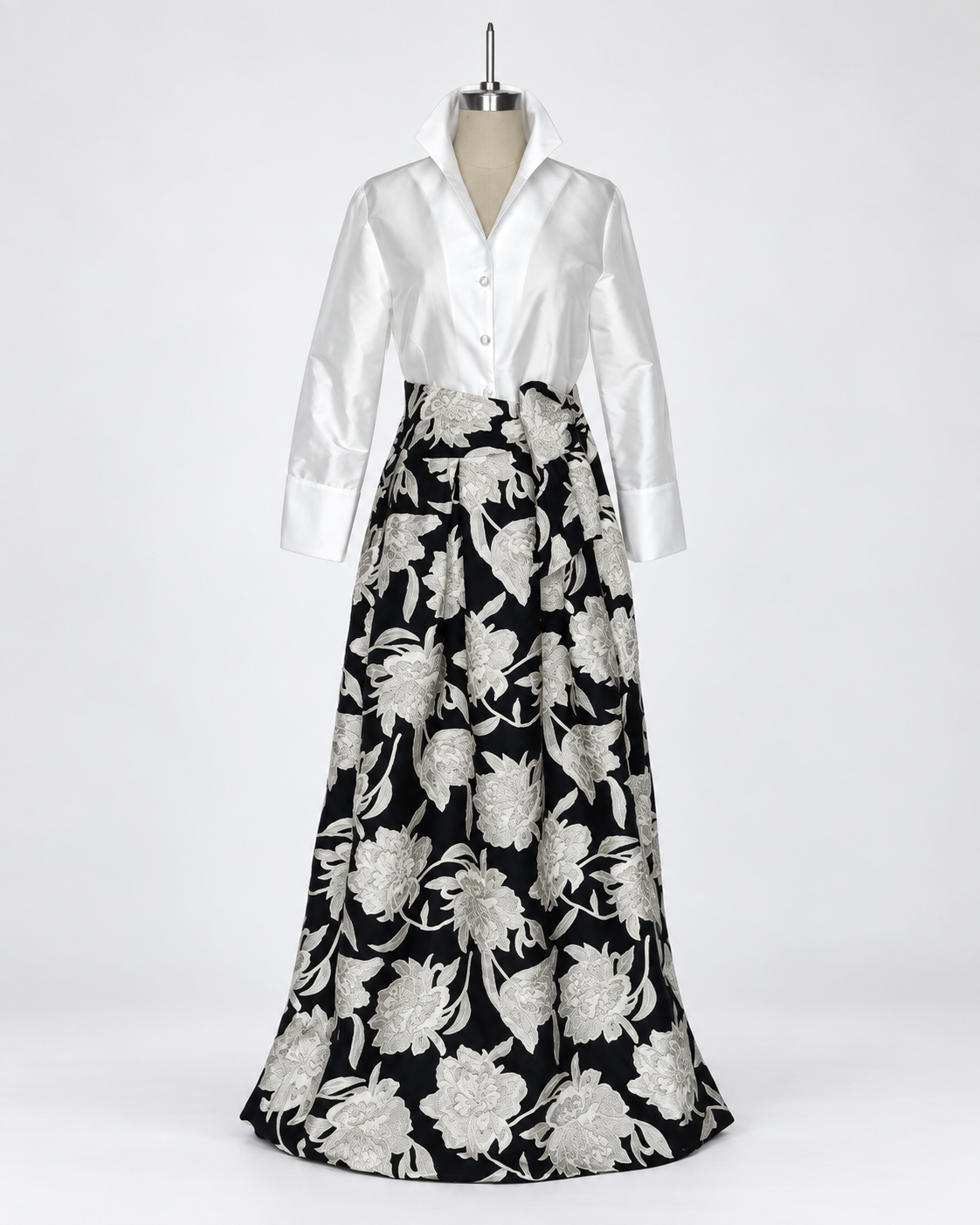 Connie Roberson Greyson Amazon Wrap Skirt A long formal dress displayed on a mannequin against a light gray studio background. The dress has a white satin long-sleeve button-front bodice and a full black skirt with large silver floral embroidery.