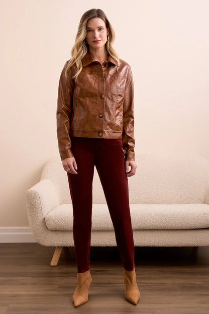 Woman wearing a brown leather jacket and red pants standing in a room with a beige couch.