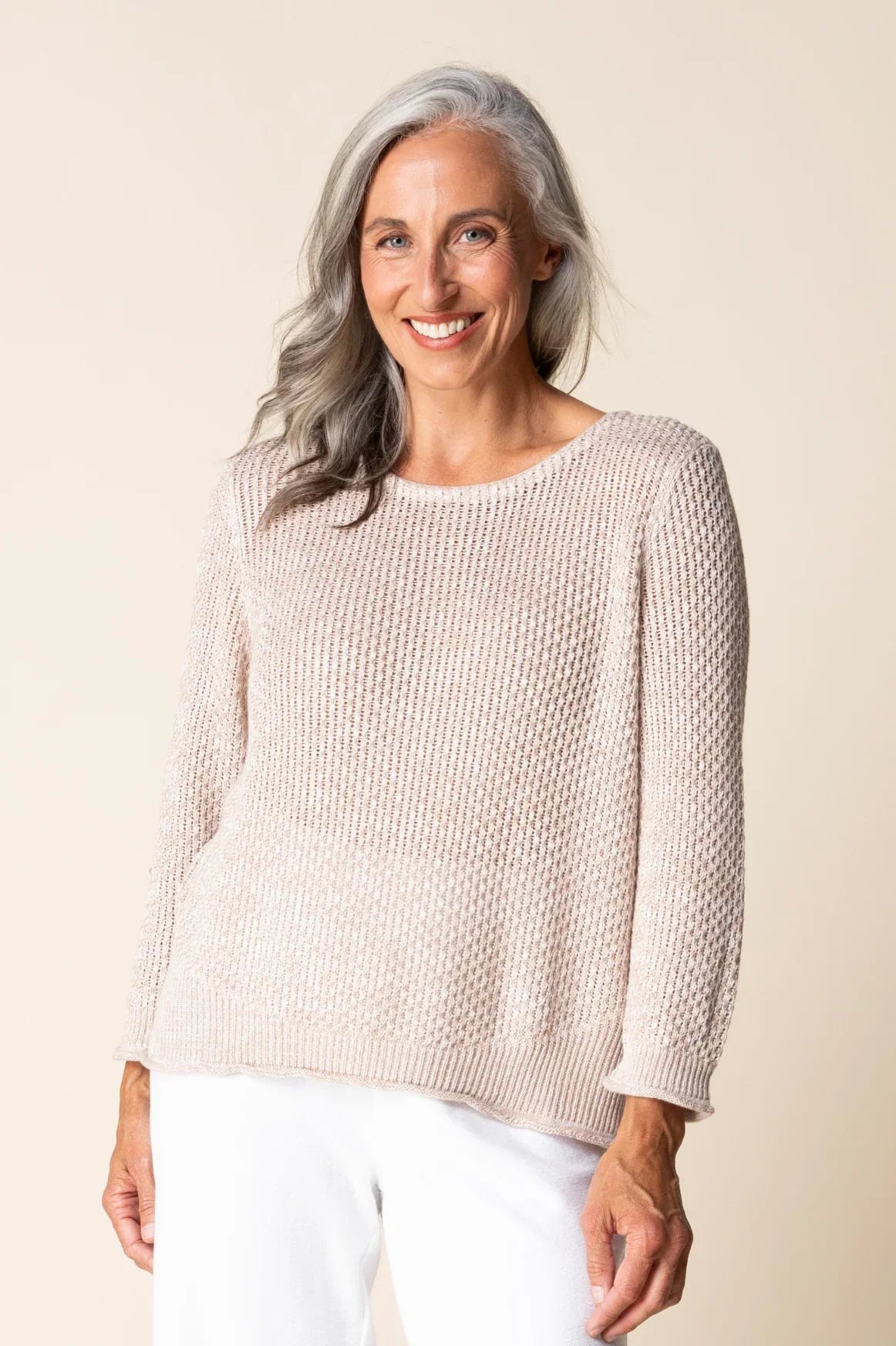 Woman wearing a beige sweater and white pants against a beige background