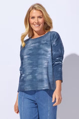 Woman wearing a blue textured top and jeans against a light gray background