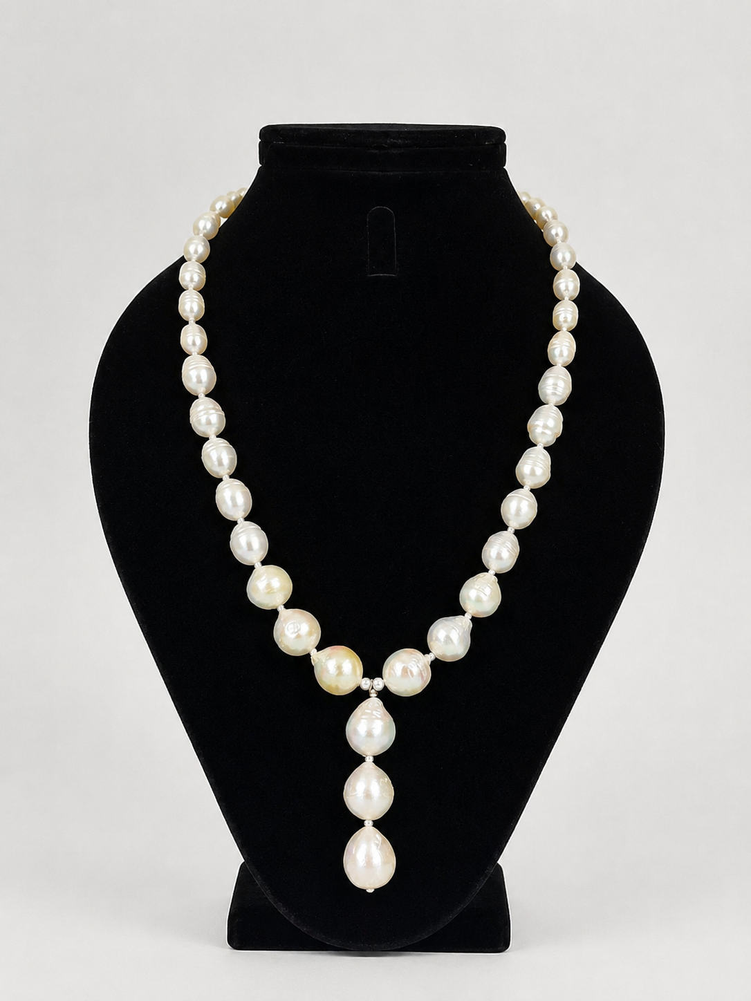 A pearl necklace features irregular white pearls with a central cluster and a teardrop-shaped pearl dangle hanging from a small silver-toned connector.