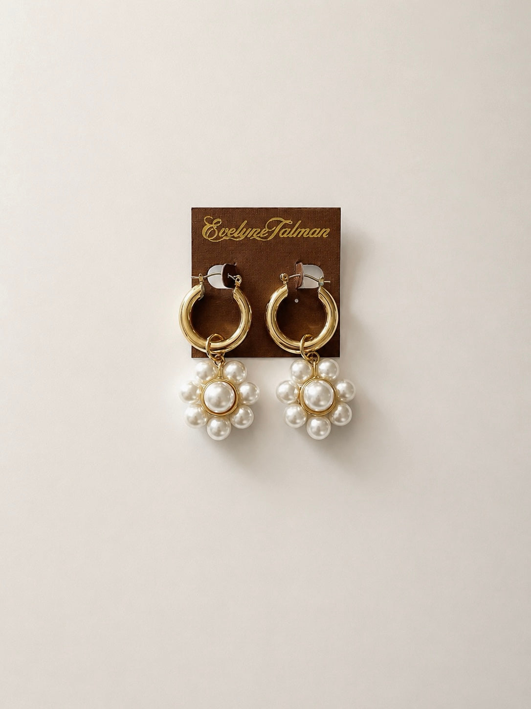 A pair of gold hoop earrings with dangling clusters of white faux pearls in  a flower shape