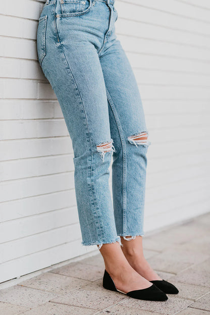 Light blue distressed jeans worn by a person against a white wall.