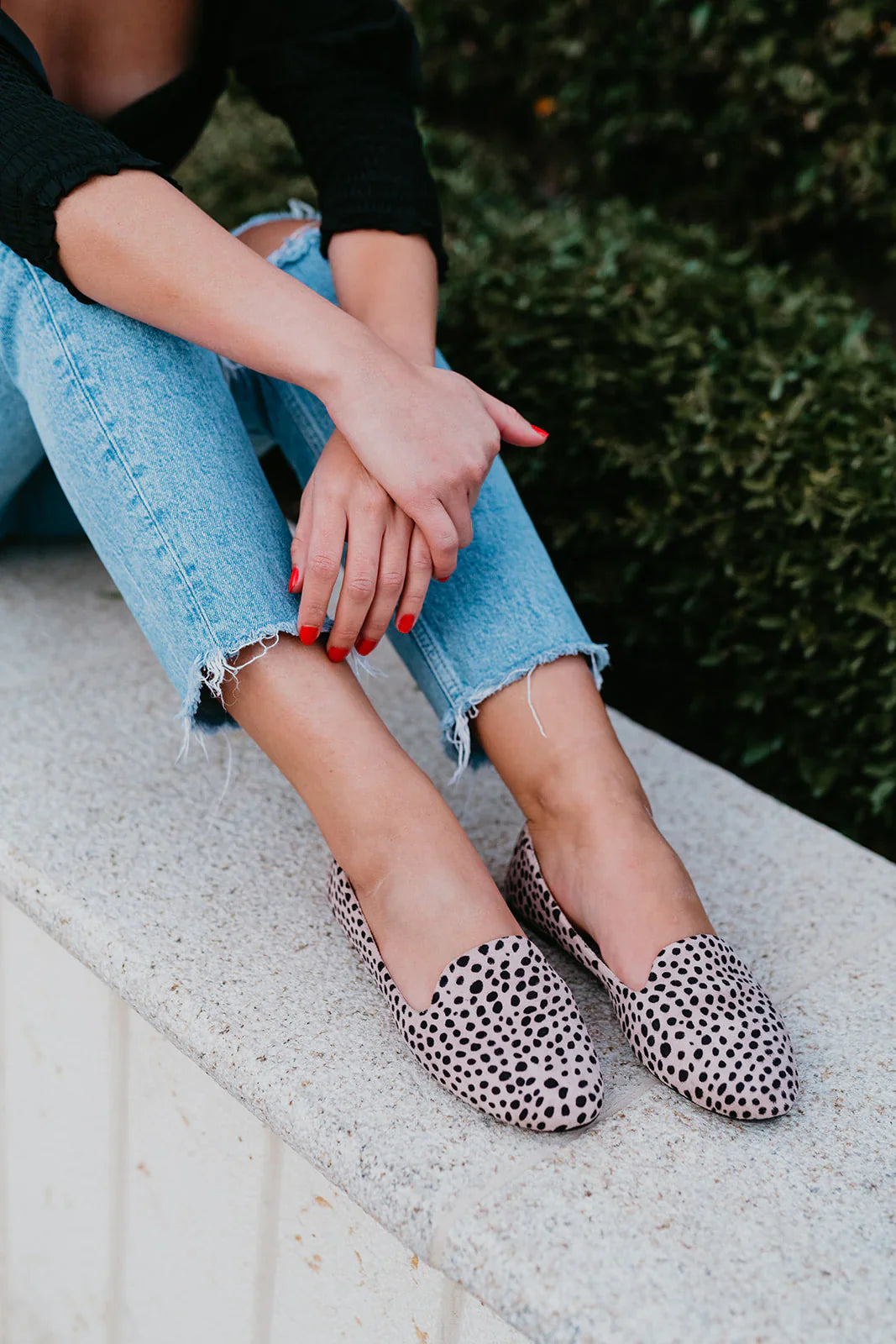 Person wearing leopard print flats and blue jeans sitting on a stone ledge.
