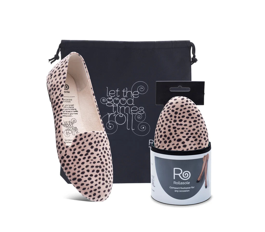 Pair of spotted ballet flats with packaging and a branded cushion on a white background