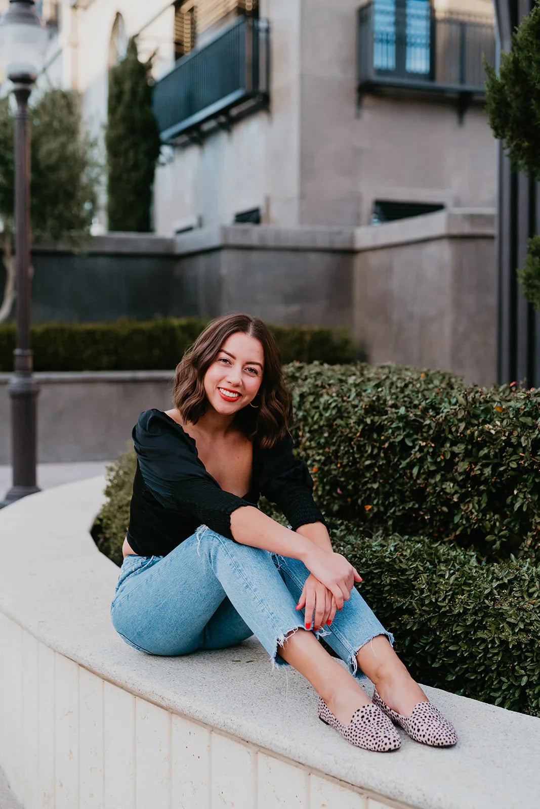 Woman sitting on a ledge outdoors with a building in the background