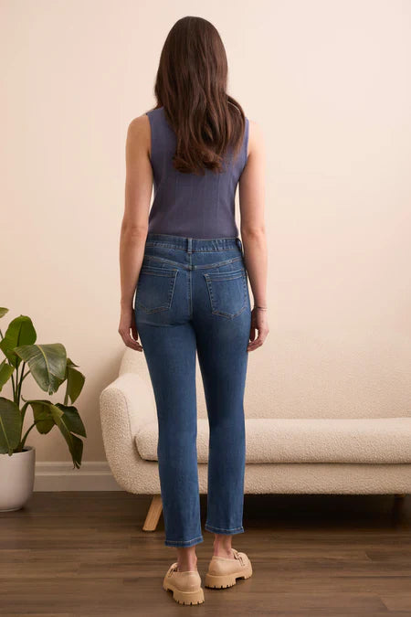 Woman wearing blue jeans standing in a room with a beige sofa and plant.