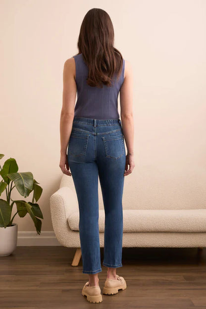 Woman wearing blue jeans standing in a room with a beige sofa and plant.