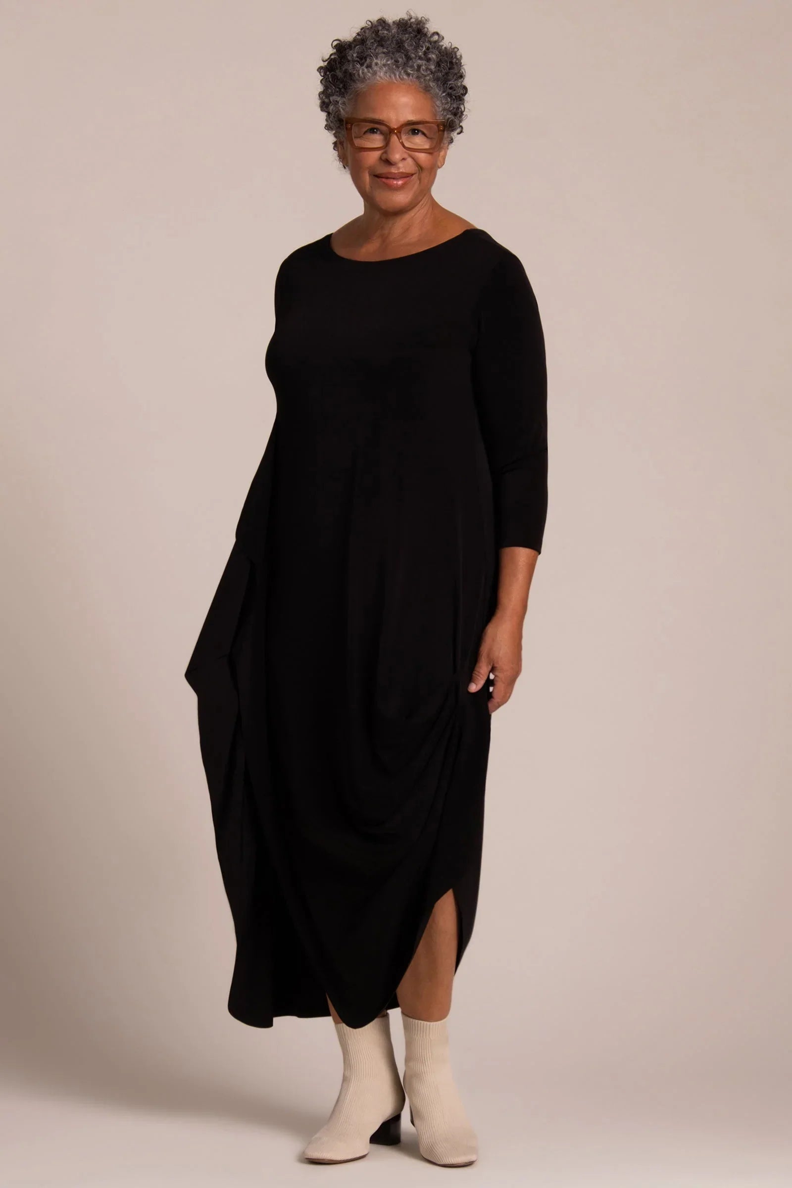 A woman modeling a black three-quarter sleeve midi dress with draped side detail and a high-low hem Sympli Drama Dress 3/4 Sleeves in Black