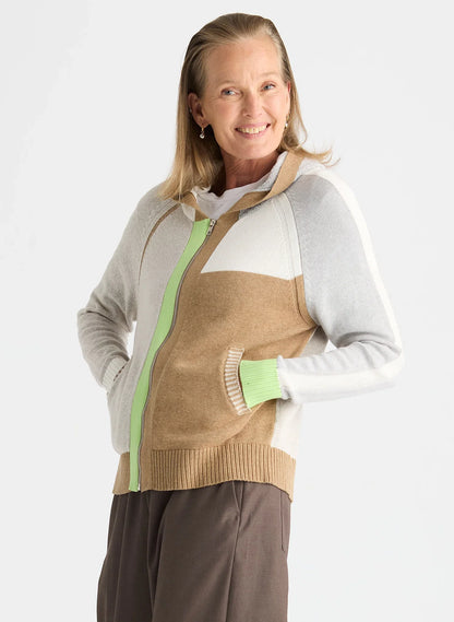 A woman modeling a color-blocked zip-up hoodie sweater with a tan body, light gray sleeves, white shoulder panels, and light green zipper and pocket accents, against a plain light gray background.