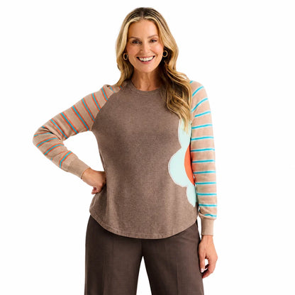 A woman modeling a long-sleeve crewneck top with a solid brown body, peach and turquoise striped sleeves, and a large light blue and coral abstract flower on the right side Zaket &amp; Plover Walnut Bright Side Sweater