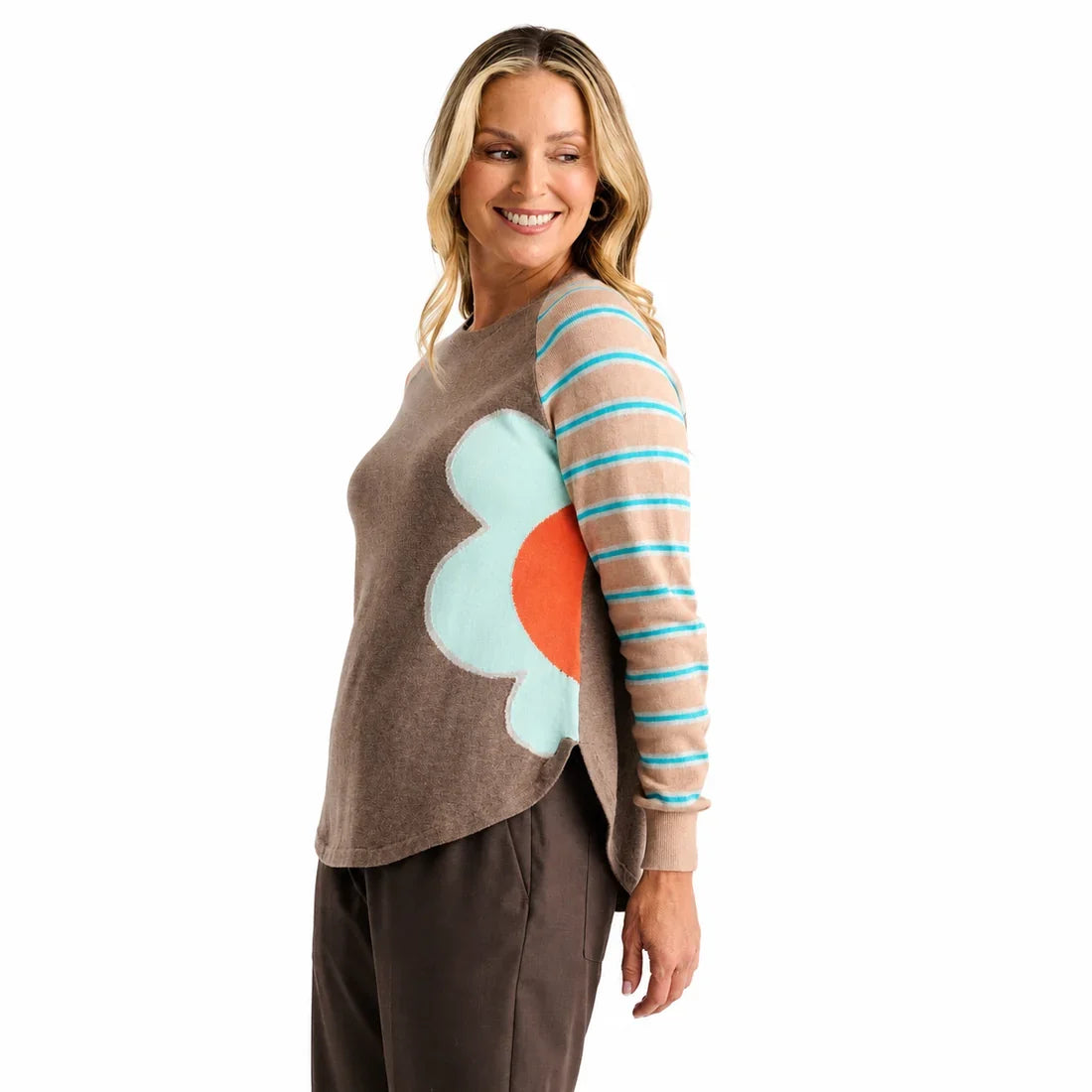 A woman modeling a long-sleeve crewneck top with a solid brown body, peach and turquoise striped sleeves, and a large light blue and coral abstract flower on the right side Zaket &amp; Plover Walnut Bright Side Sweater