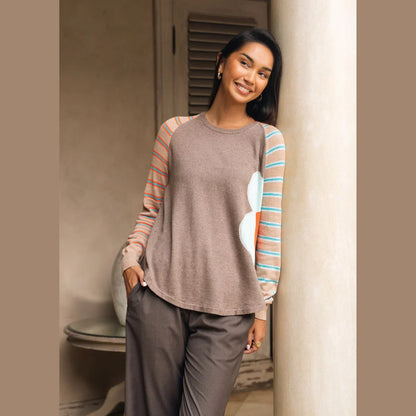 A woman modeling a long-sleeve crewneck top with a solid brown body, peach and turquoise striped sleeves, and a large light blue and coral abstract flower on the right side Zaket &amp; Plover Walnut Bright Side Sweater
