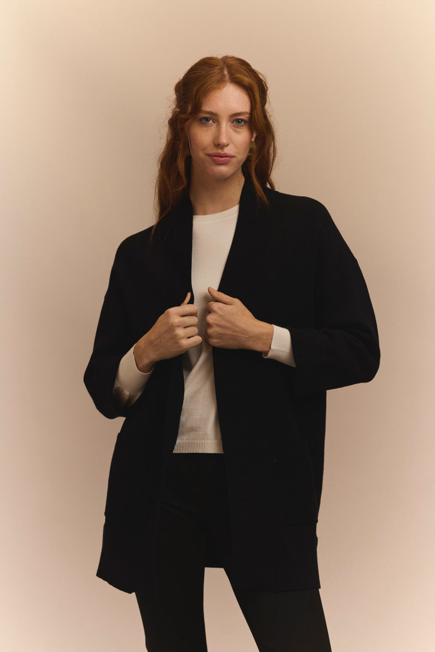 Woman wearing a black cardigan over a white shirt on a beige background