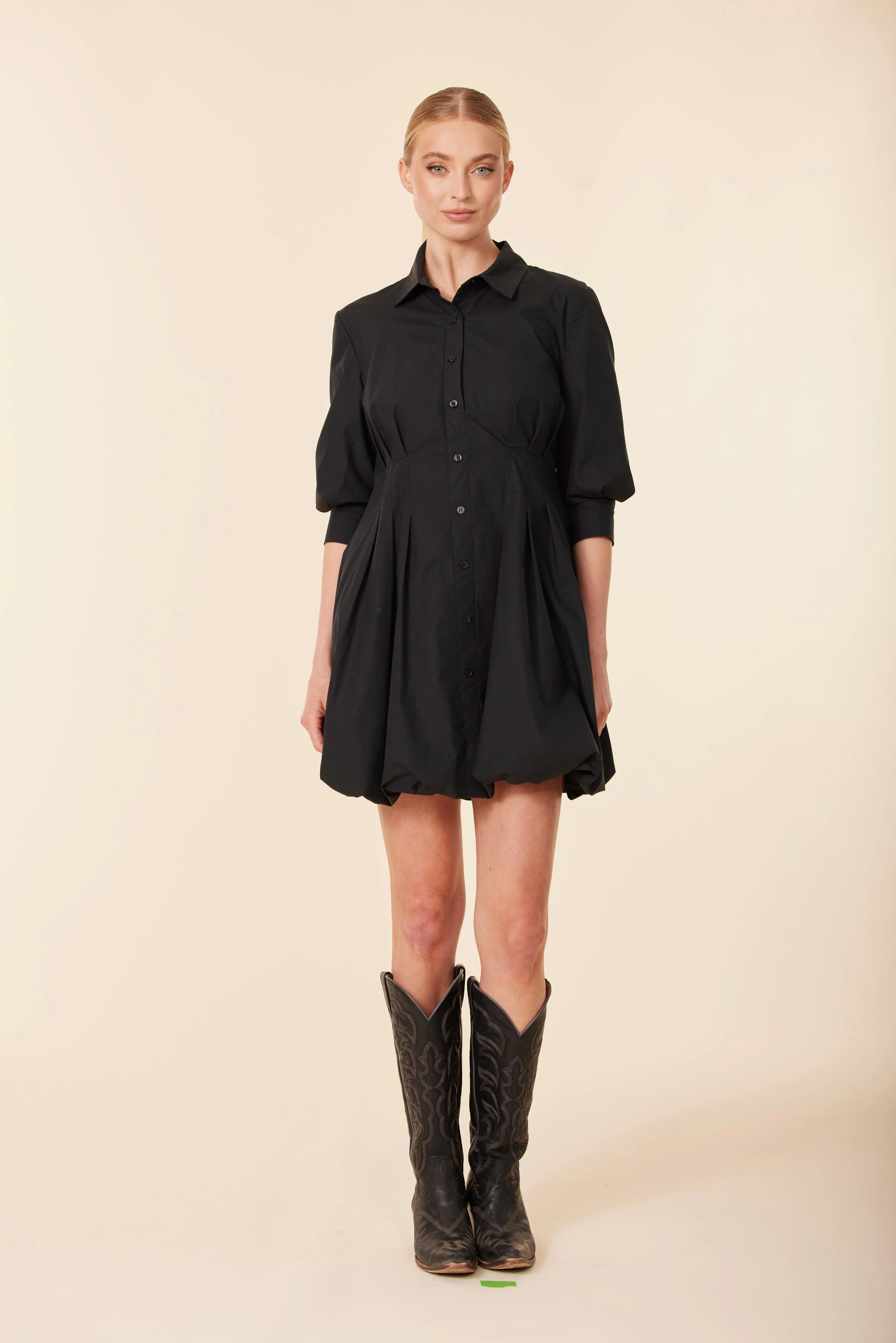 Woman wearing a black dress and cowboy boots on a beige background