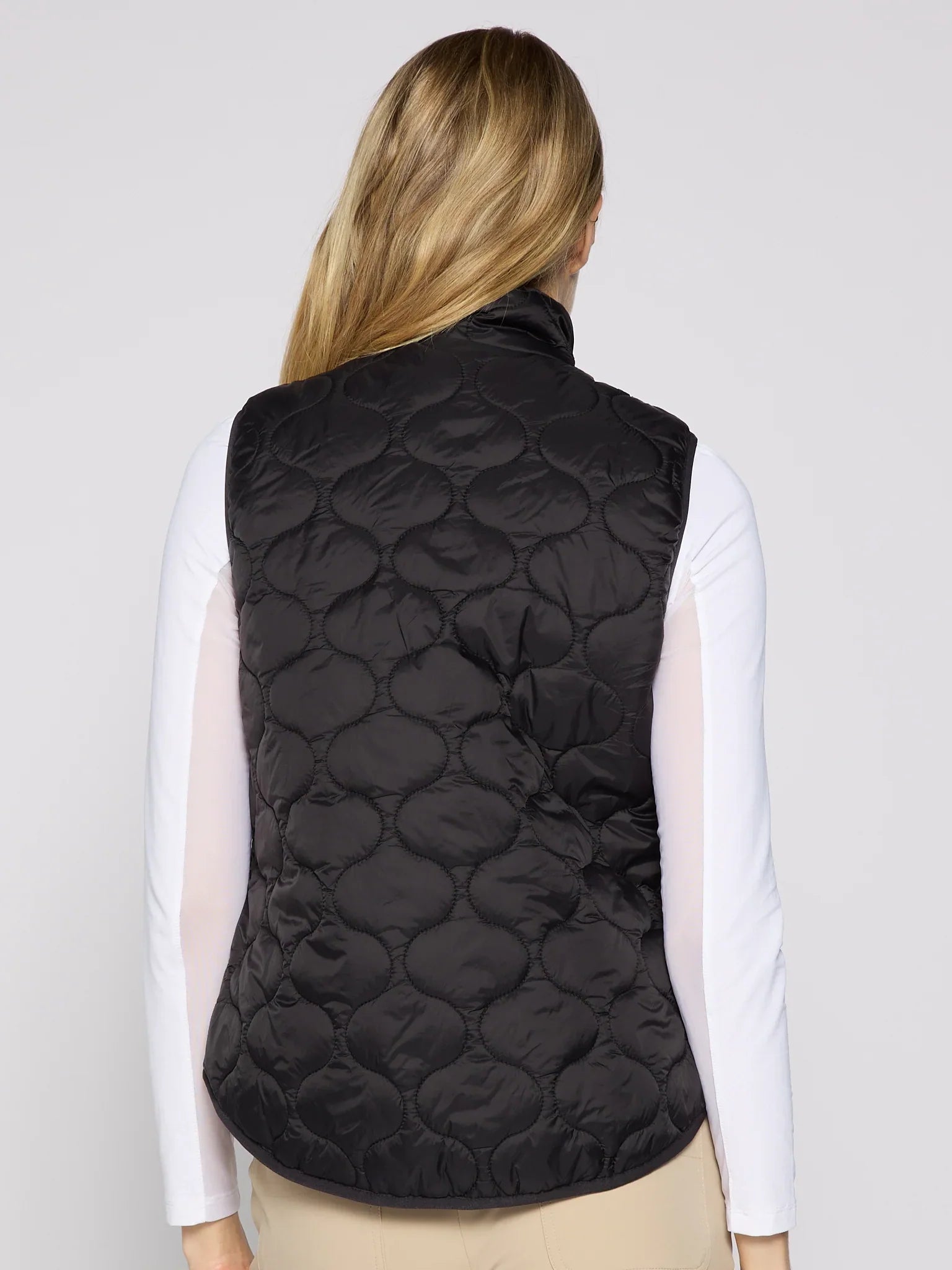 Person wearing a black quilted vest on a plain background