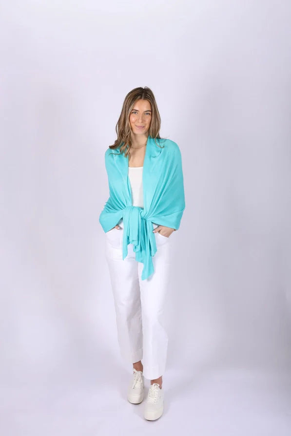 Woman wearing a turquoise Ari Bamboo Shawl Wrapover a white top and pants on a white background