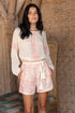 Woman wearing a white and pink patterned outfit standing against a textured wall.