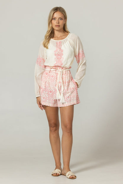 Woman wearing a white blouse with pink floral patterns and matching shorts on a plain background