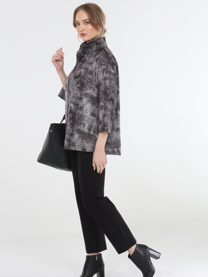 Woman wearing a patterned gray top and black pants on a white background